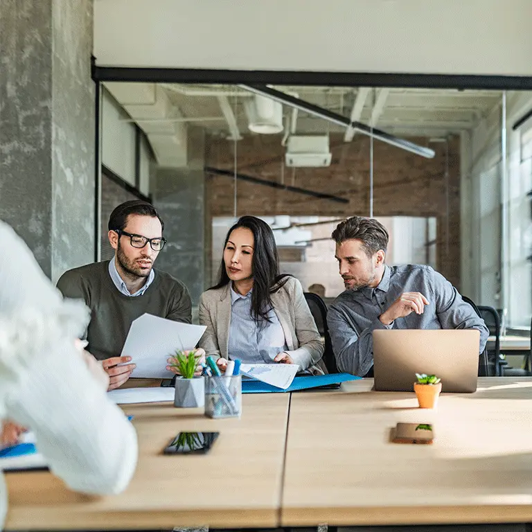 co workers gathered around a laptop looking at paper reports